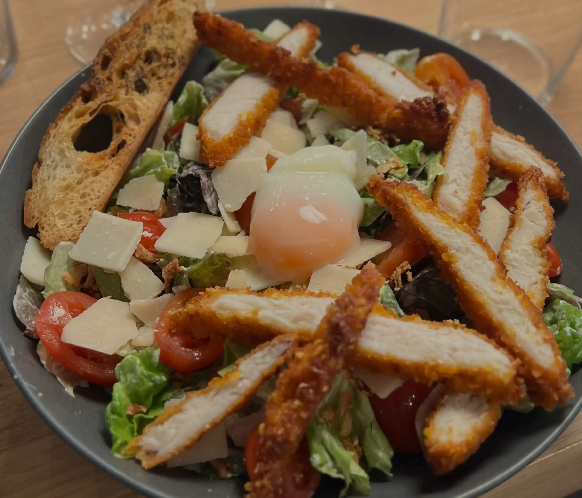 Une salade Caesar : lanières de poulet pané, œuf mollet, copeaux de fromage, tomates cerises et croûton.