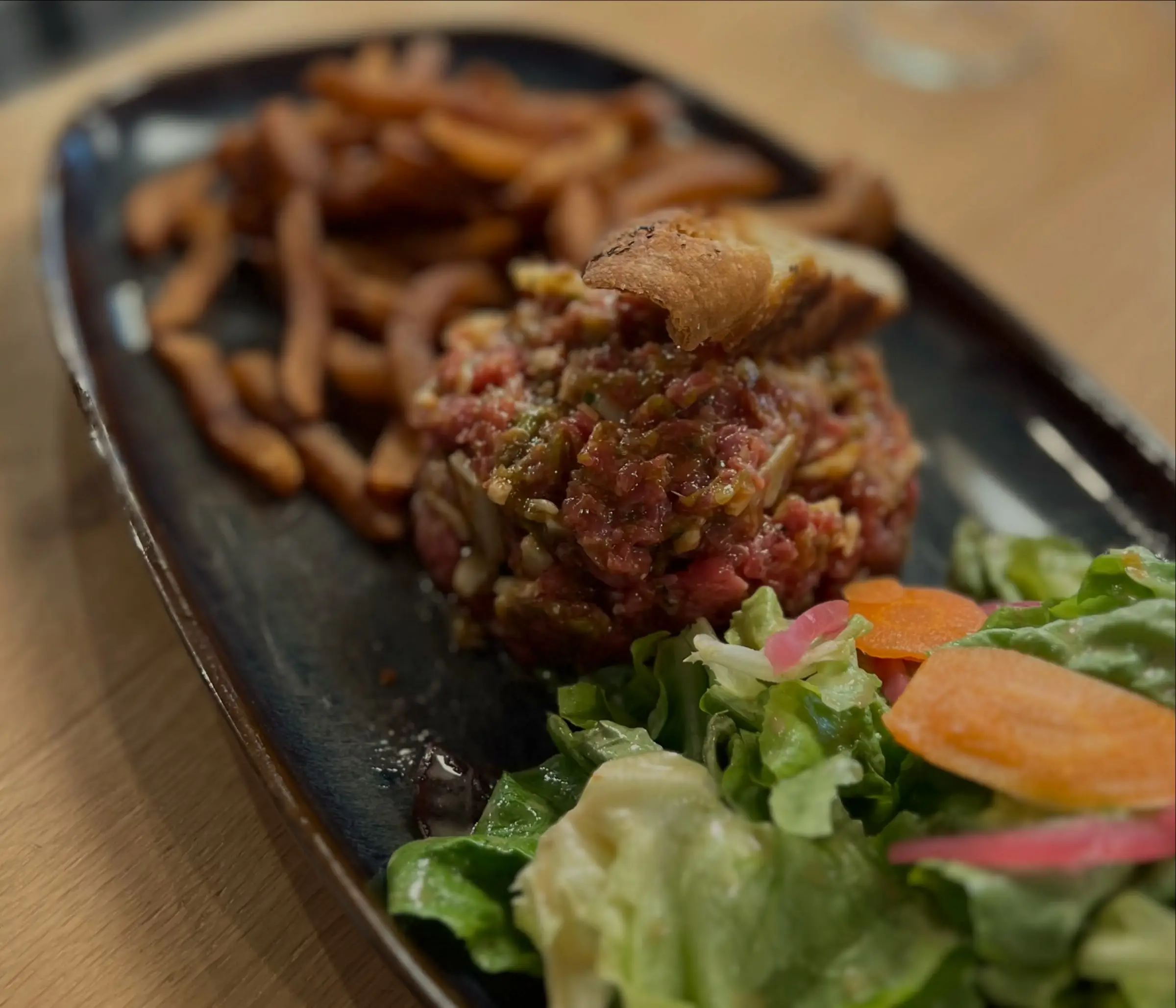 Un tartare de bœuf au couteau, avec son croûton, des frites et de la salade.