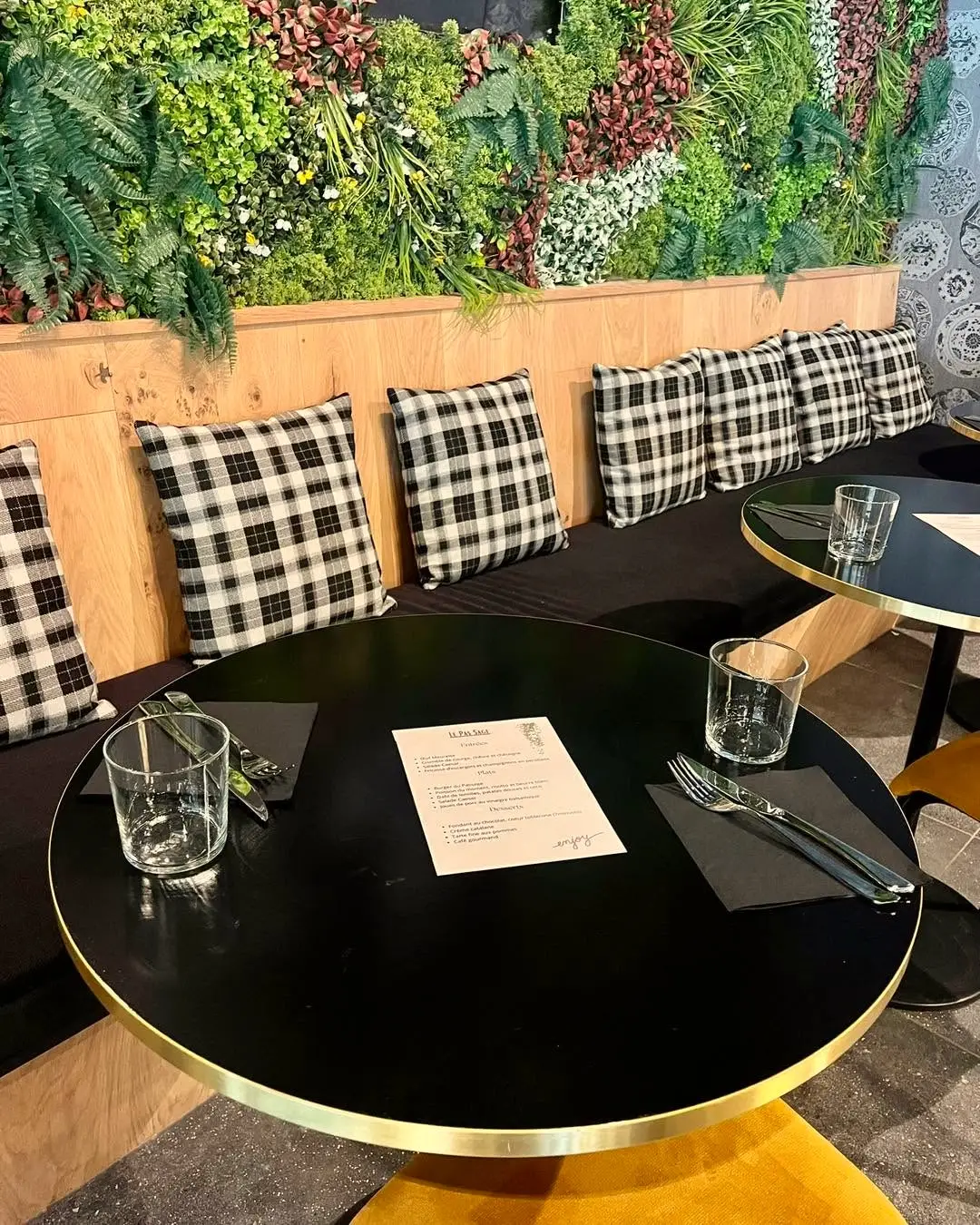 Une banquette à coussins à carreaux, sous le mur végétal.